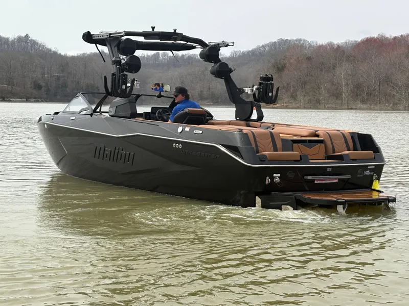 Slide: The Image of 2025 Malibu 25 LSV boat cruising on a calm lake with wooded shoreline. - 12