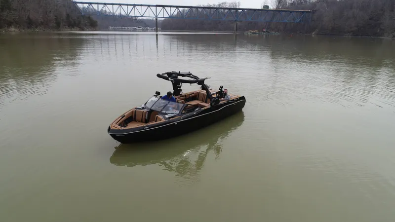 Slide: The Image of 2025 Malibu 25 LSV boat on calm river with bridge in background. - 17