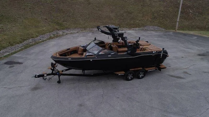 Slide: The Image of 2025 Malibu 25 LSV boat on trailer, black exterior, brown interior, parked on pavement. - 18