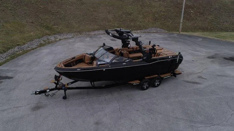 Slide: The Image of 2025 Malibu 25 LSV boat on trailer, black exterior, parked on paved surface. - 22