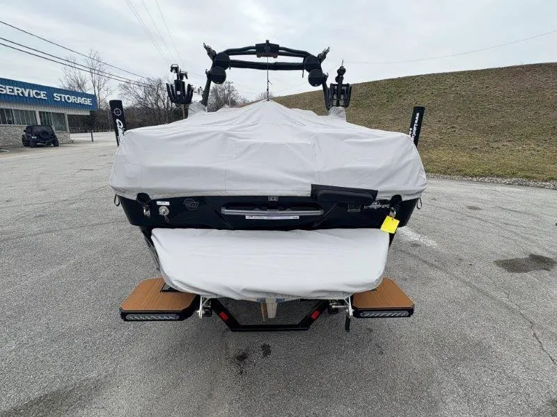 Slide: The Image of 2025 Malibu 25 LSV boat covered, parked outdoors near service storage facility. - 28