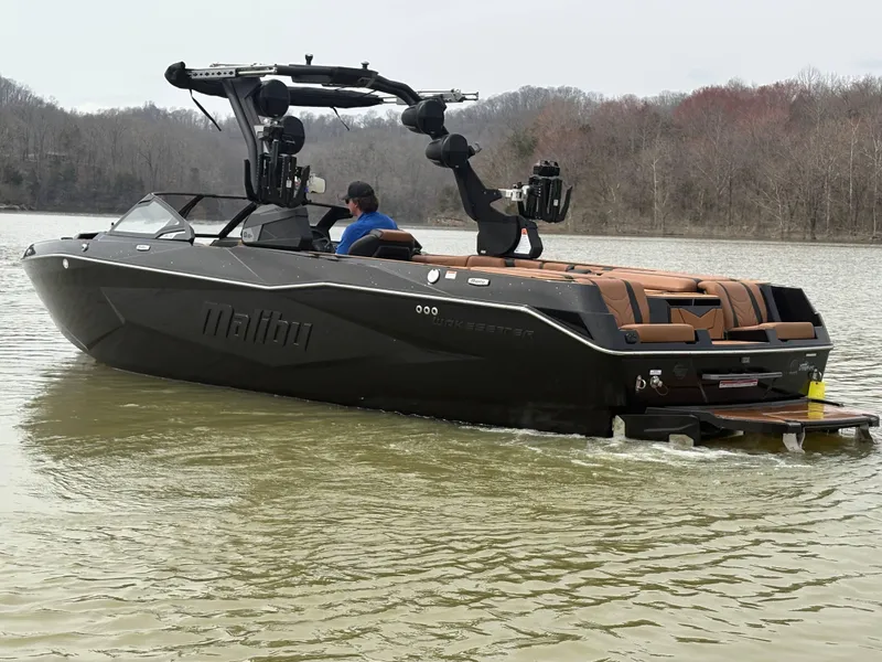 Slide: The Image of 2025 Malibu 25 LSV boat on a calm lake with wooded shoreline. - 9