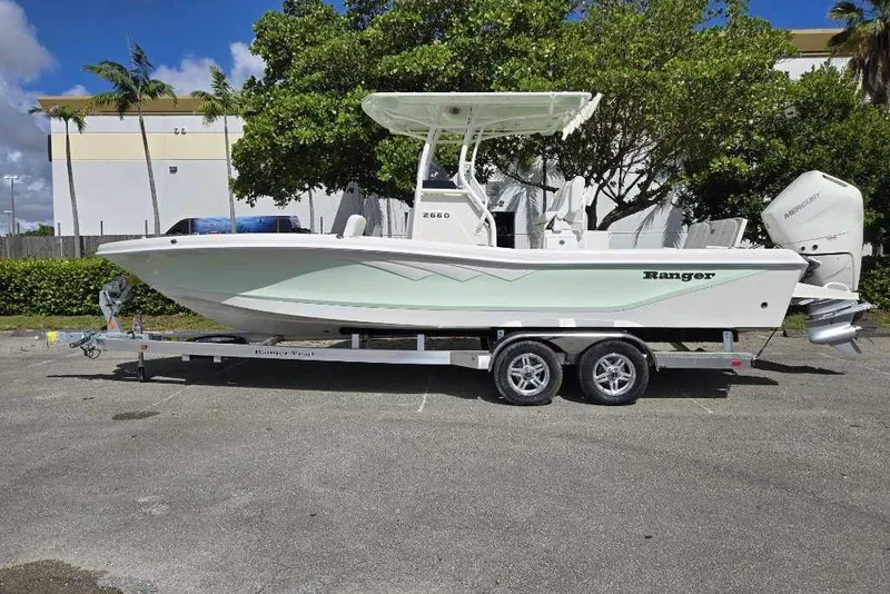 Slide: The Image of 2025 Ranger 2660 Bay boat on trailer, parked outdoors, with trees and building in background. - 0