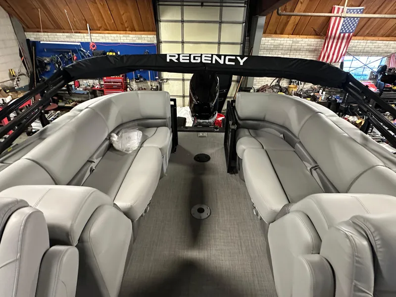 Slide: The Image of 2025 Regency 230 DL3 pontoon boat interior with gray seating in a garage setting. - 11