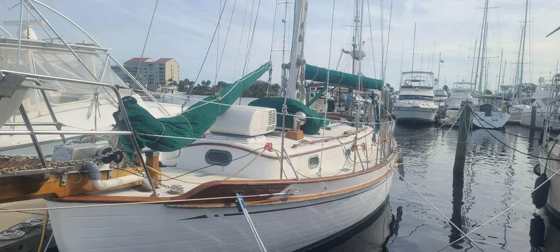 The Image of 1985 Tayana 37 sailboat docked in marina, green covers, calm water. - 0