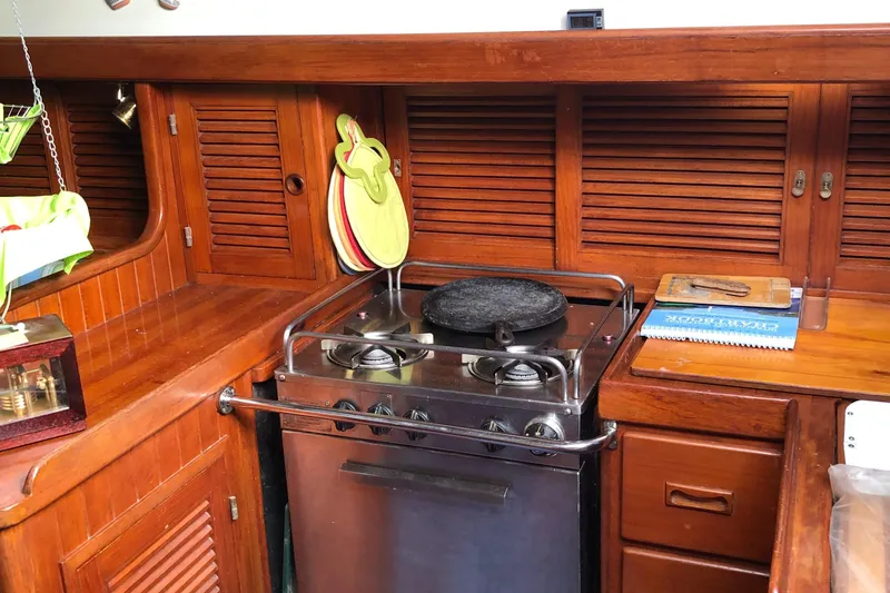 Slide: The Image of 1985 Tayana 37 yacht kitchen with wooden cabinets and a stainless steel stove. - 11