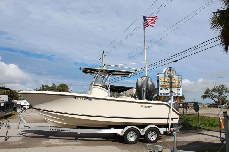 The Image of 2008 Pursuit C230 boat on trailer, parked near a sign and American flag. - 0