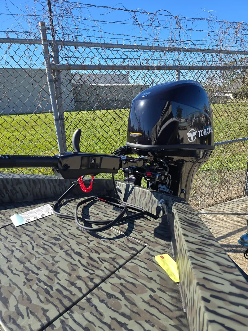 Slide: The Image of 2025 Edge Duck Boats 753 DB with Tohatsu outboard motor, camo design, parked by a fence. - 4