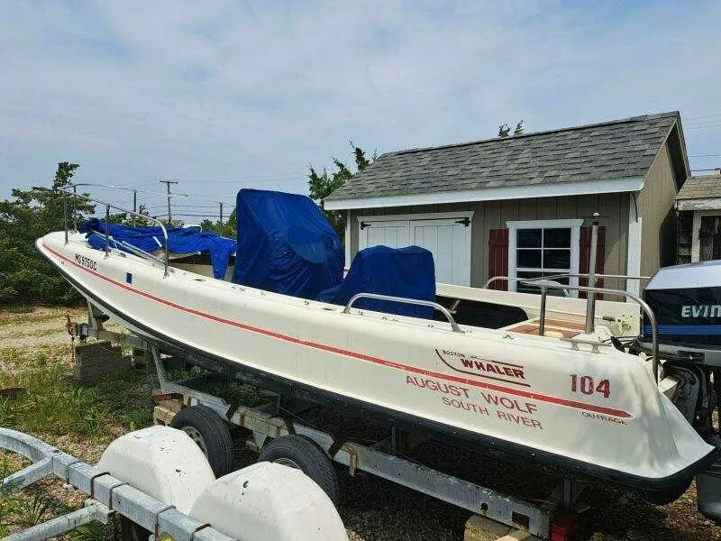 Slide: The Image of 1973 Boston Whaler 21 Outrage boat on trailer, parked near a small building. - 17