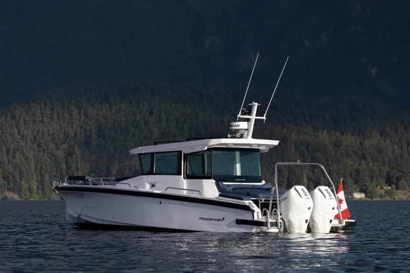 Slide: The Image of 2025 Axopar 29 XC boat on a serene lake with forested mountains in the background. - 2