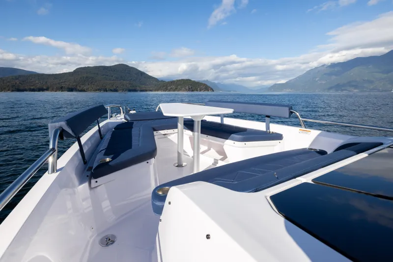 Slide: The Image of 2025 Axopar 29 XC boat interior with seating and table, scenic mountain and water view. - 7