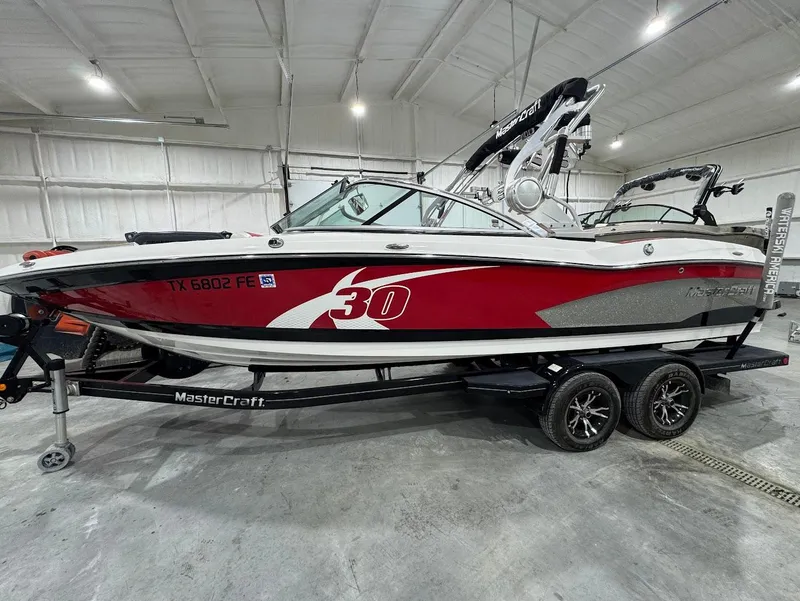 Slide: The Image of 2013 MasterCraft X30 boat in a garage, red and white design, on a trailer. - 1