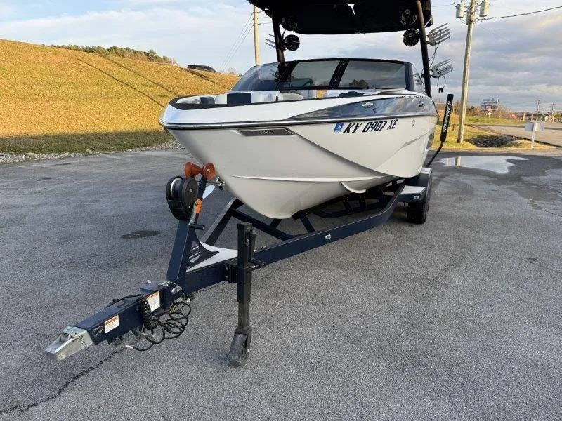 Slide: The Image of 2021 Malibu 25 LSV boat on trailer, parked on asphalt, under cloudy sky. - 23