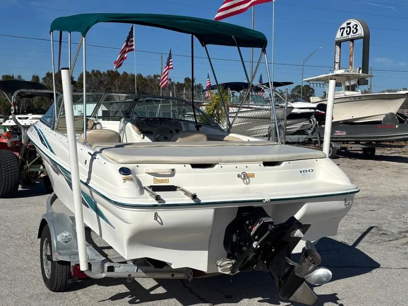 Slide: The Image of 1998 Sea Ray 180 Bow Rider boat with canopy, parked on trailer, flags in background. - 4