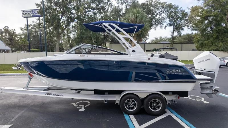 Slide: The Image of 2025 Cobalt R6 Outboard boat on trailer, blue and white design, parked outdoors. - 4