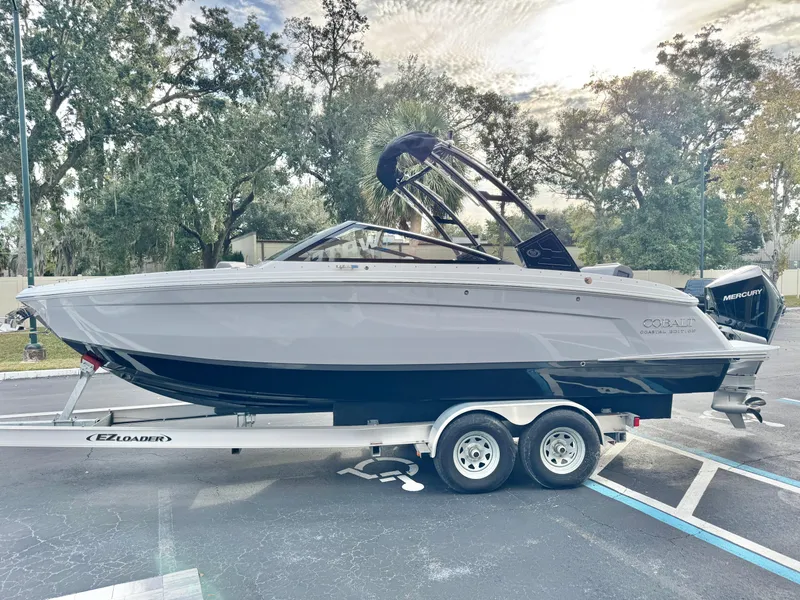 Slide: The Image of 2025 Cobalt R6 Outboard boat on trailer, parked outdoors with trees in background. - 10
