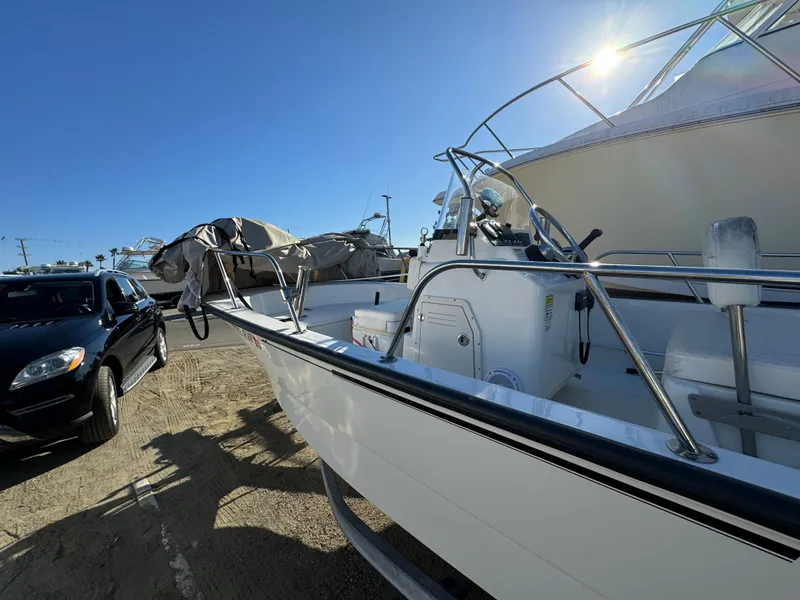 Slide: The Image of 2016 Boston Whaler 170 MONTUCK boat parked beside a black car under clear blue sky. - 13