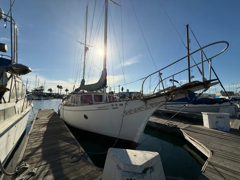 The Image of 1973 Islander 40 sailboat docked at marina, sun shining through mast, calm waters. - 1