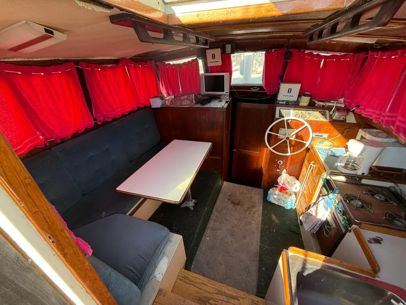 Slide: The Image of Interior of a 1973 Islander 40 sailboat with red curtains and a cozy seating area. - 10