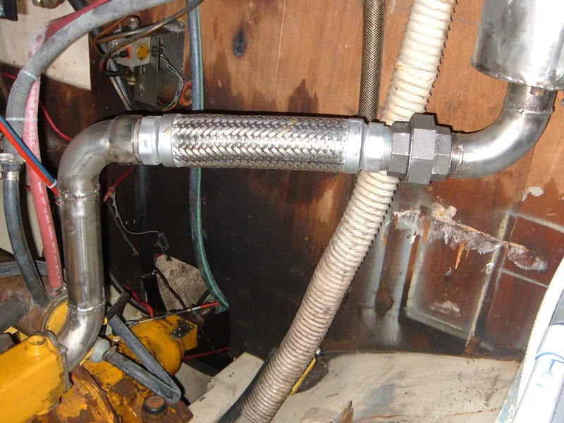 Slide: The Image of Engine compartment of a 1973 Islander 40 sailboat, featuring metal exhaust piping and braided hose. - 21