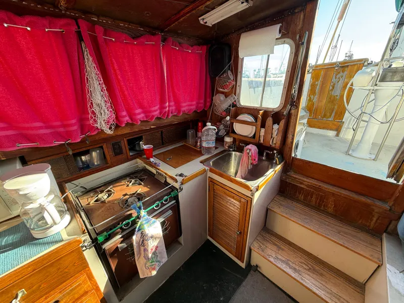 Slide: The Image of 1973 Islander 40 yacht kitchen with stove, sink, and vibrant red curtains. - 8