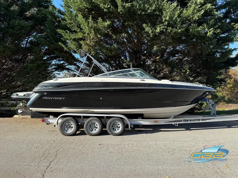 Slide: The Image of 2013 Monterey 264FS boat on trailer, parked outdoors, surrounded by trees. - 2