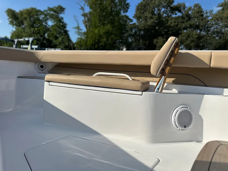 Slide: The Image of 2024 Jupiter 43 boat interior with beige seating and speaker, surrounded by trees. - 26