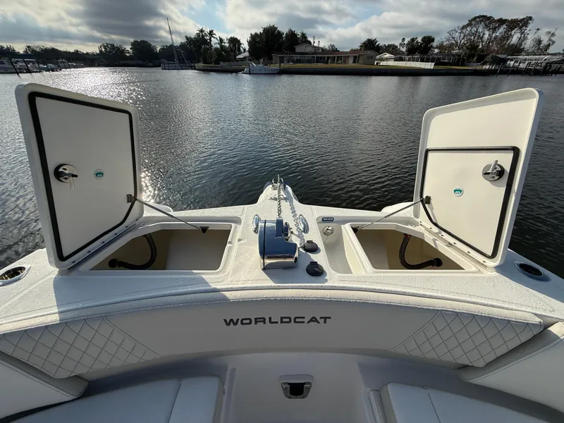 Slide: The Image of 2025 World Cat 325 DC boat with open storage compartments on a calm lake. - 12