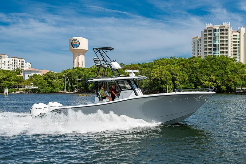 Slide: The Image of 2024 Costa Custom Boats 34 cruising on water near cityscape and greenery. - 109