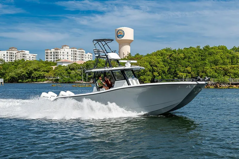 Slide: The Image of 2024 Costa Custom Boats 34 cruising on water near lush greenery and buildings. - 110