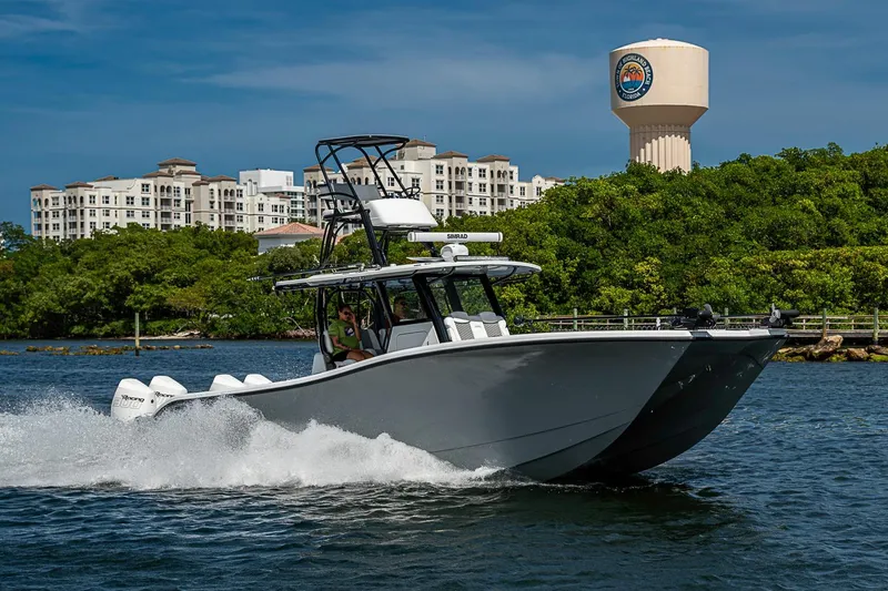 Slide: The Image of 2024 Costa Custom Boats 34 cruising on water near lush greenery and buildings. - 112