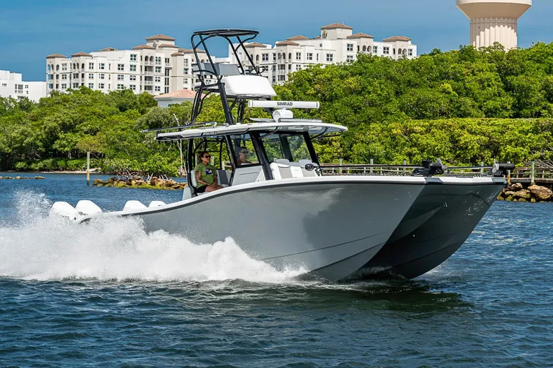 Slide: The Image of 2024 Costa Custom Boats 34 cruising on water near lush greenery and modern buildings. - 113