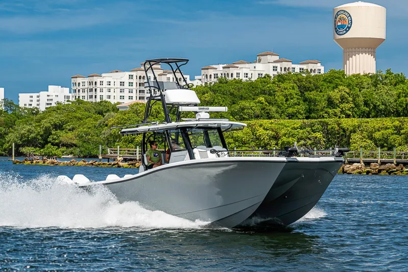 Slide: The Image of 2024 Costa Custom Boats 34 cruising on water near lush greenery and buildings. - 114