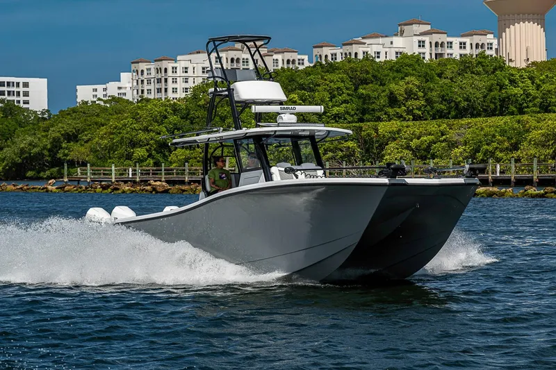 Slide: The Image of 2024 Costa Custom Boats 34 cruising on water near lush greenery and buildings. - 115