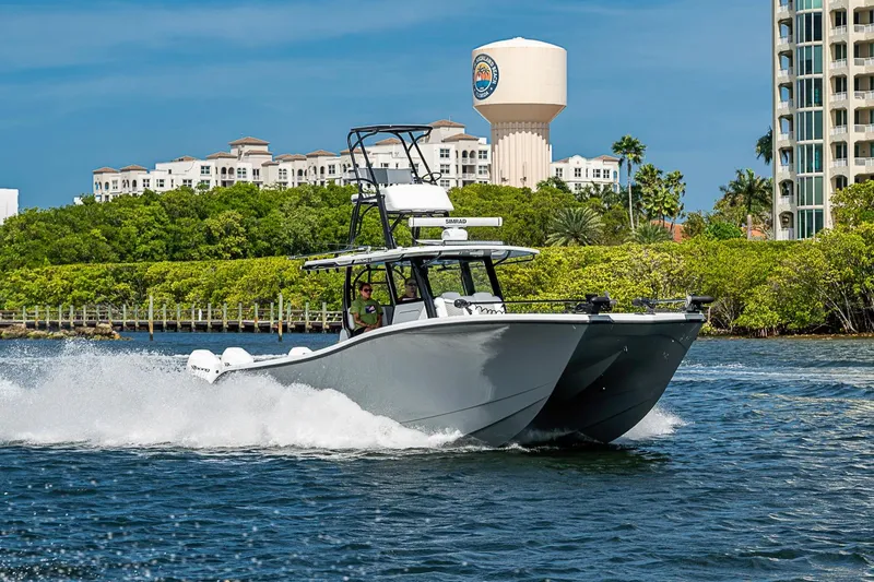 Slide: The Image of 2024 Costa Custom Boats 34 cruising on water near lush greenery and buildings. - 116