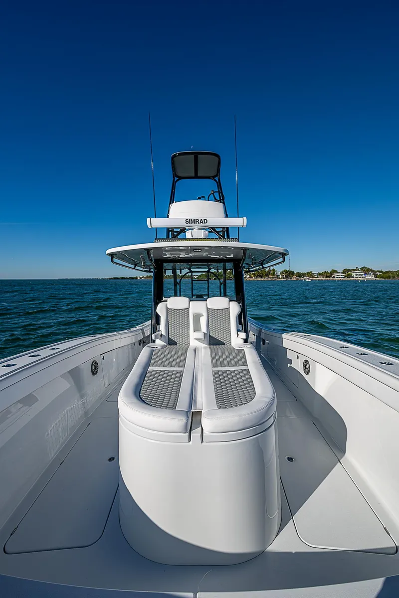Slide: The Image of 2024 Costa Custom Boats 34 cruising on water near lush greenery and buildings. - 99