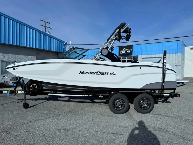 Slide: The Image of 2025 MasterCraft NXT20 boat on trailer, parked outside a blue building. - 1