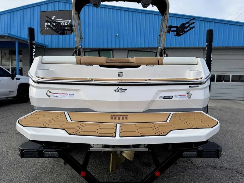 Slide: The Image of 2025 MasterCraft NXT20 boat rear view with teak deck, parked outside a blue building. - 8