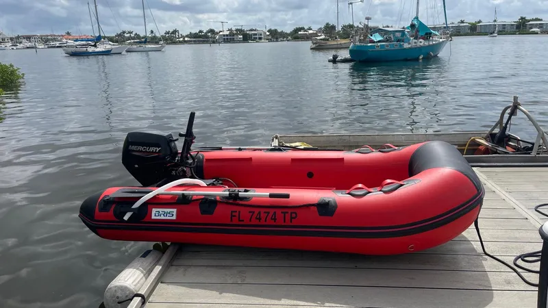 Slide: The Image of Red inflatable boat with Mercury motor docked by a marina, surrounded by sailboats. - 12