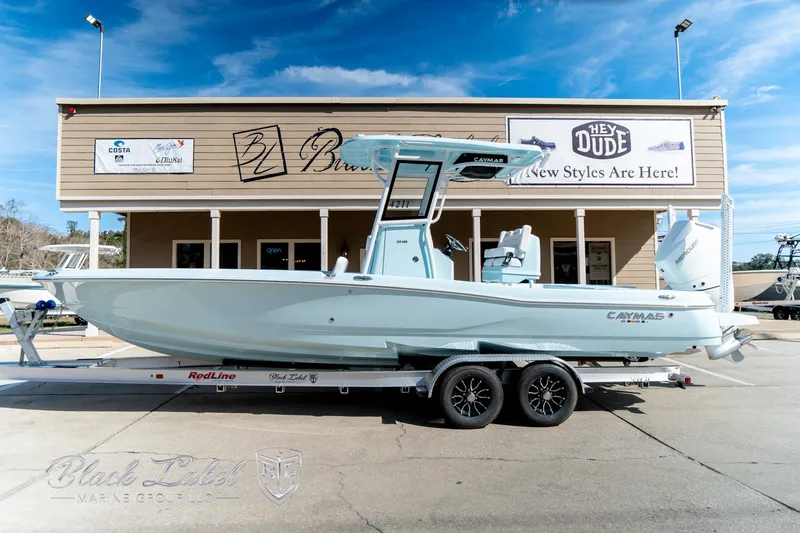 Slide: The Image of 2025 Caymas 28 HB boat on trailer, parked outside a building under a clear blue sky. - 1