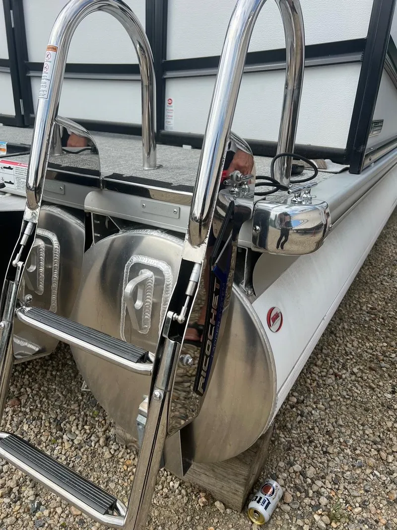 Slide: The Image of 2024 Premier 230 SunSation RF pontoon boat ladder and pontoons on gravel surface. - 8