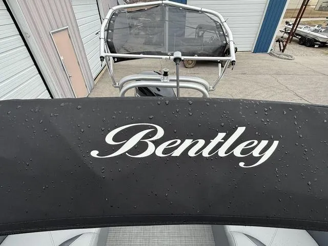 Slide: The Image of 2025 Bentley Pontoons Legacy 243 Navigator with raindrops on cover, docked near storage units. - 20