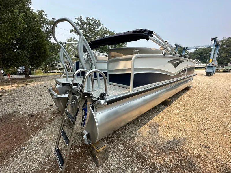 Slide: The Image of 2023 Premier 250 Solaris RF pontoon boat with ladder, parked on gravel. - 2