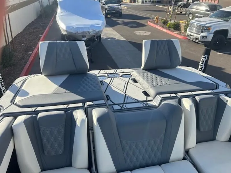 Slide: The Image of 2025 Malibu M230 boat interior with gray and white seating, parked outdoors. - 24