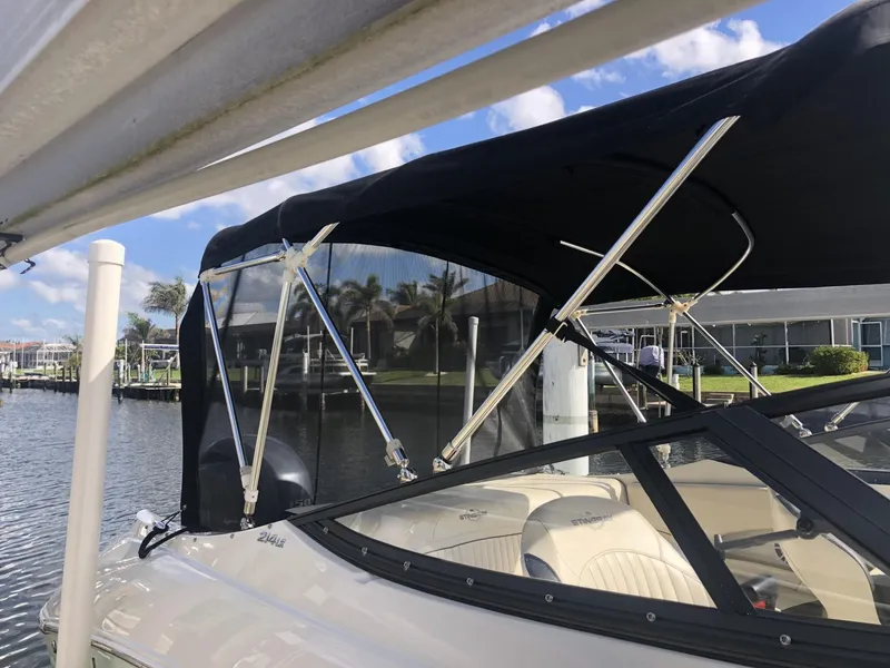 Slide: The Image of 2021 Stingray 214 LR boat with black canopy docked by waterfront homes. - 12