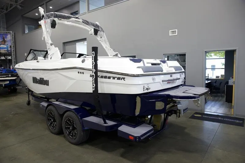 Slide: The Image of 2025 Malibu 23 LSV boat in showroom, white and blue design, on trailer. - 4