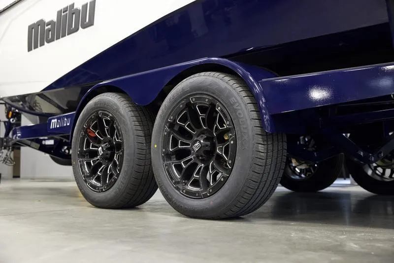 Slide: The Image of 2025 Malibu 23 LSV boat trailer with black wheels in a showroom. - 7