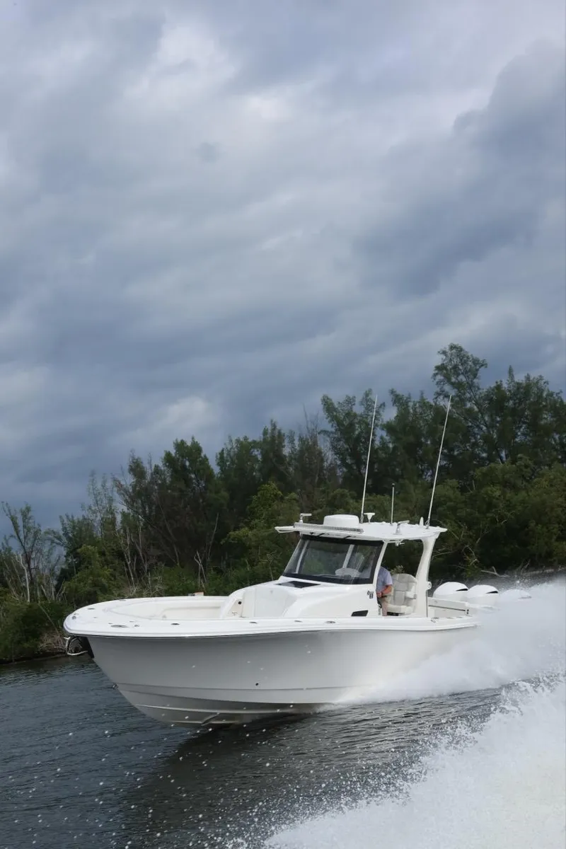 Slide: The Image of 2019 Edgewater 370CC boat cruising on a cloudy day near lush greenery. - 5