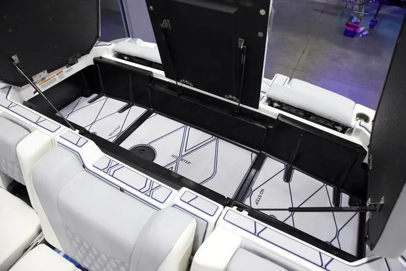 Slide: The Image of 2025 Malibu M242 boat storage compartment with open hatches and cushioned seating. - 2
