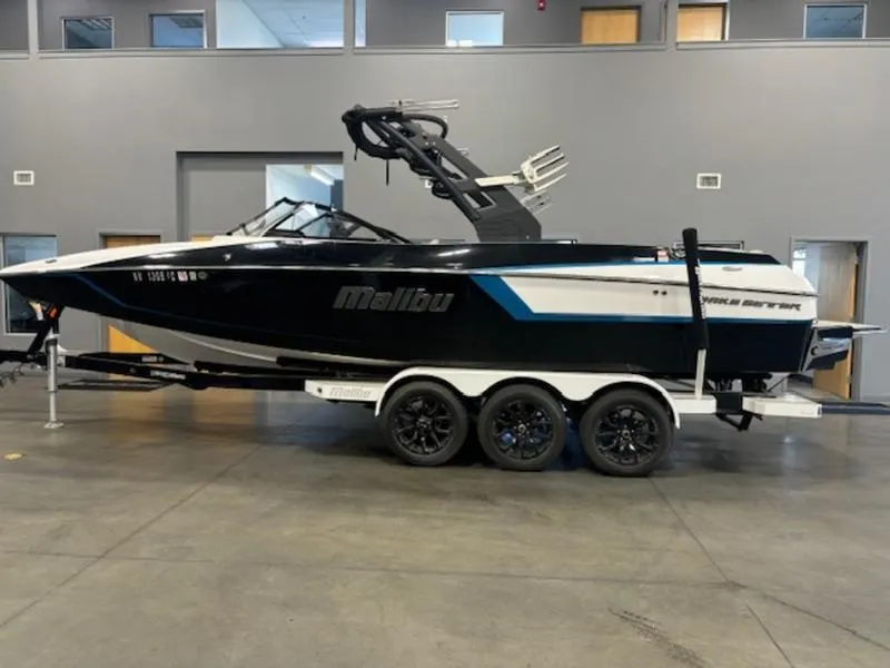 Slide: The Image of 2025 Malibu 24 MXZ boat on trailer in showroom, sleek black and white design. - 1